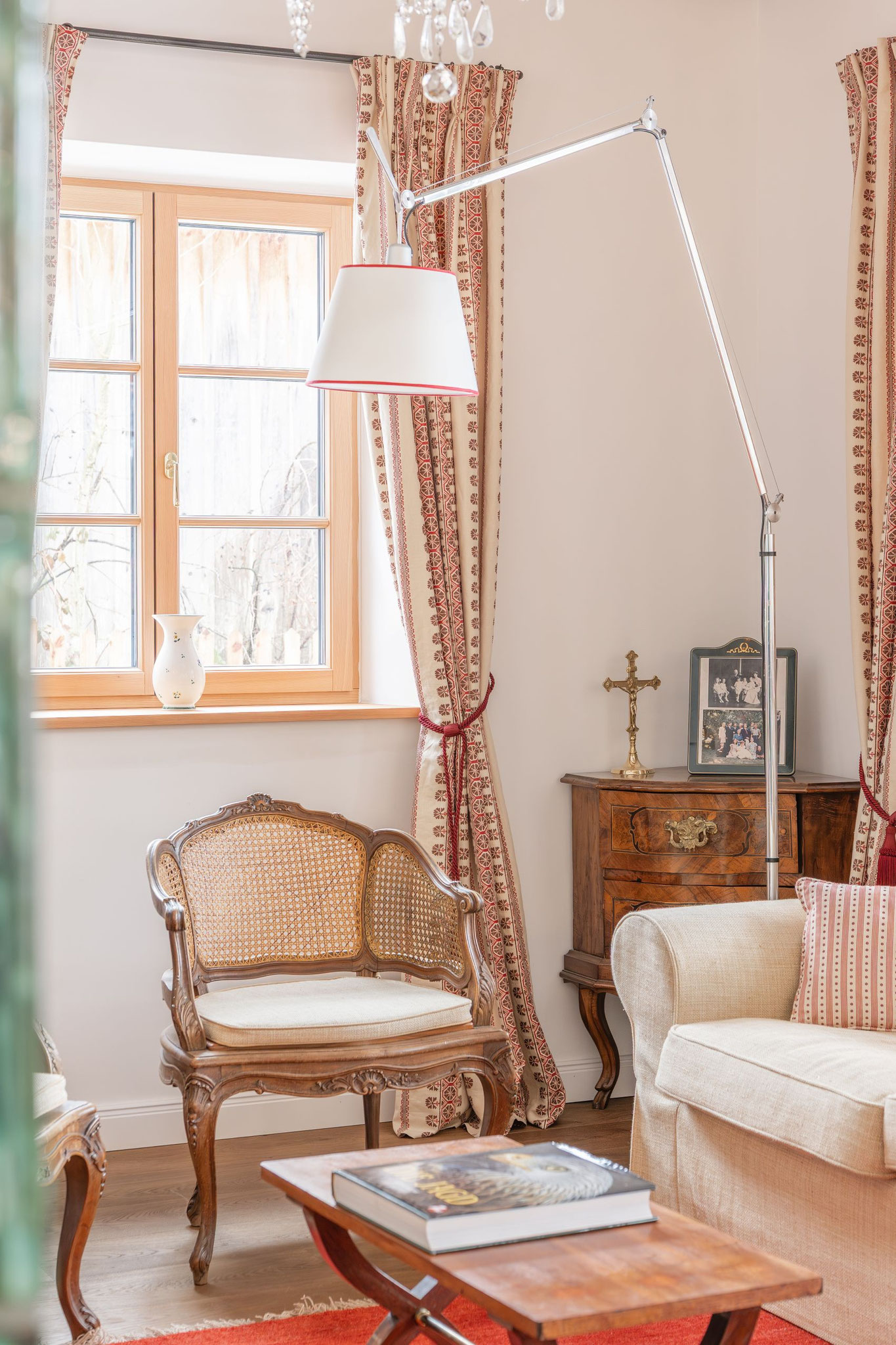 Gemütliche Leseecke mit Rattansessel, Biedermeier-Kommode und gerahmten Familienfotos