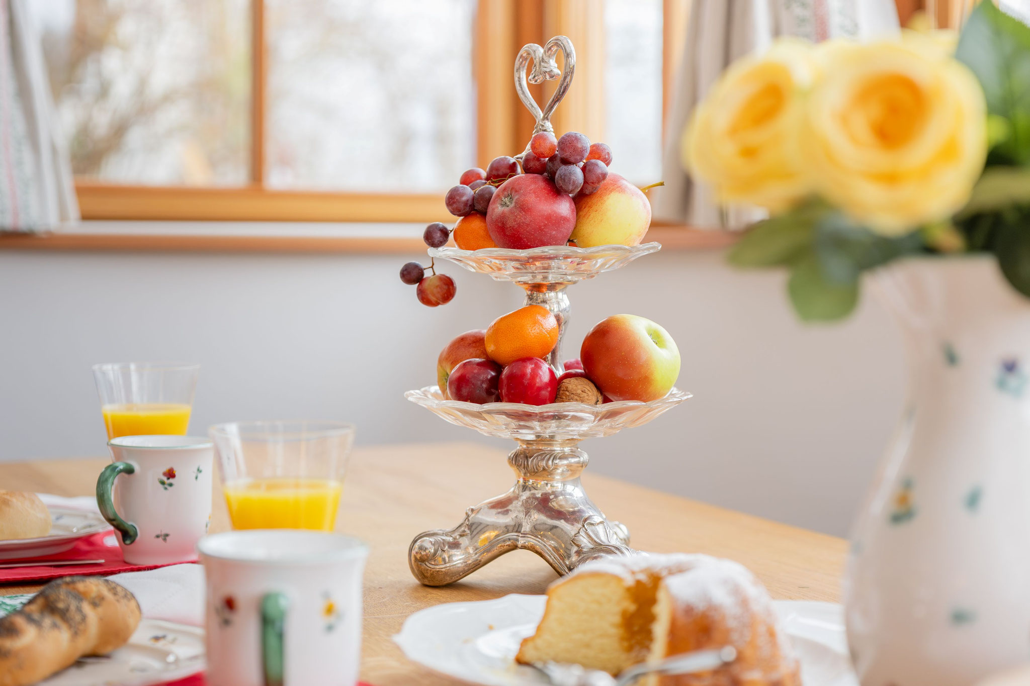 Gedeckter Frühstückstisch mit Kristall-Obstetagere, Gugelhupf und gelben Rosen