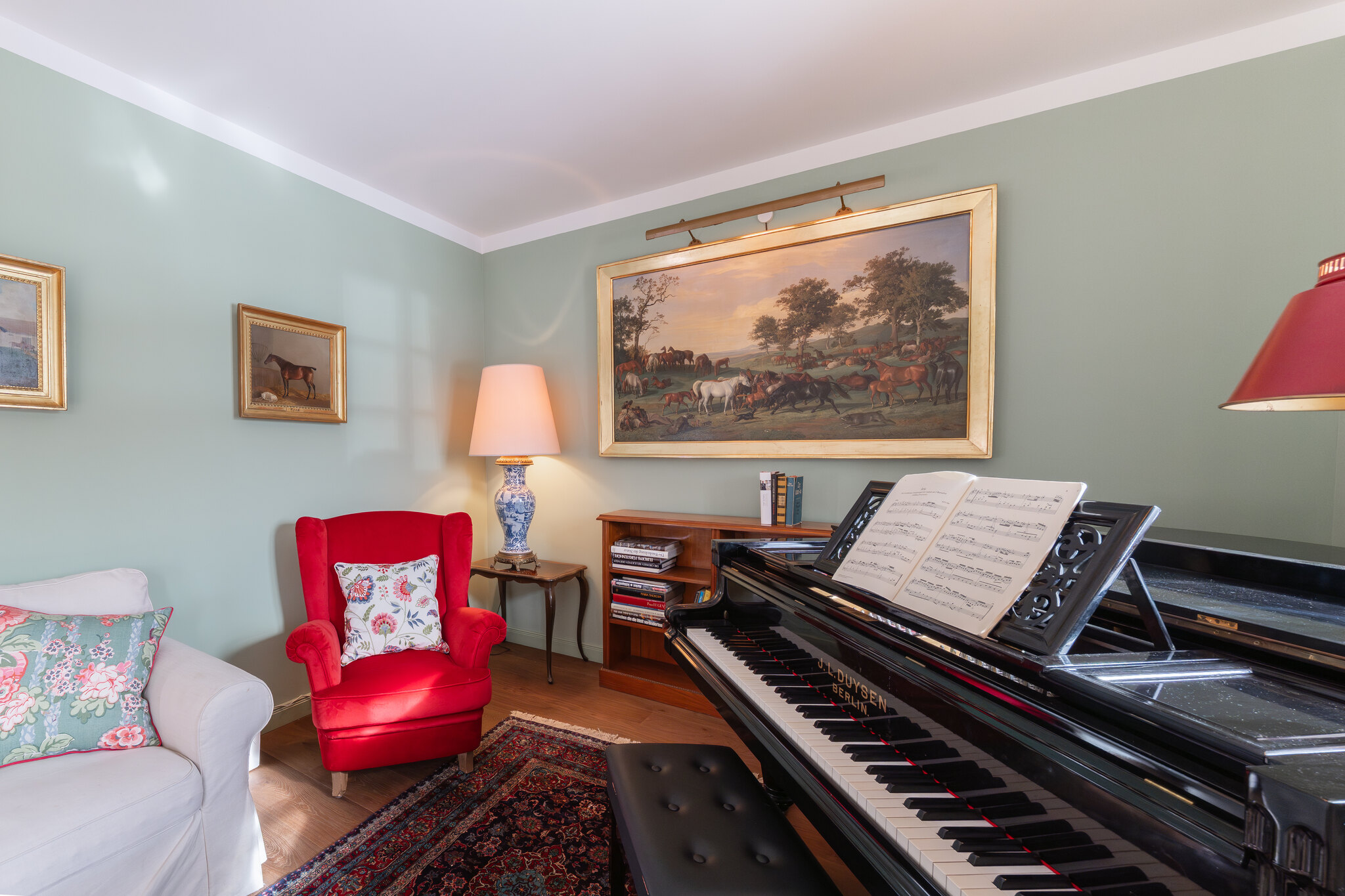 Musikzimmer im Gästehaus Eltz mit Duysen-Stutzflügel von 1930, rotem Ohrensessel und alten Gemälden