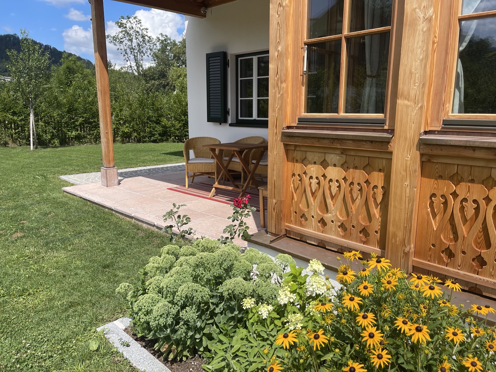 Überdachte Terrasse des Gästehaus Eltz mit Korbsesseln, Blumenbeet und Sommerwiese